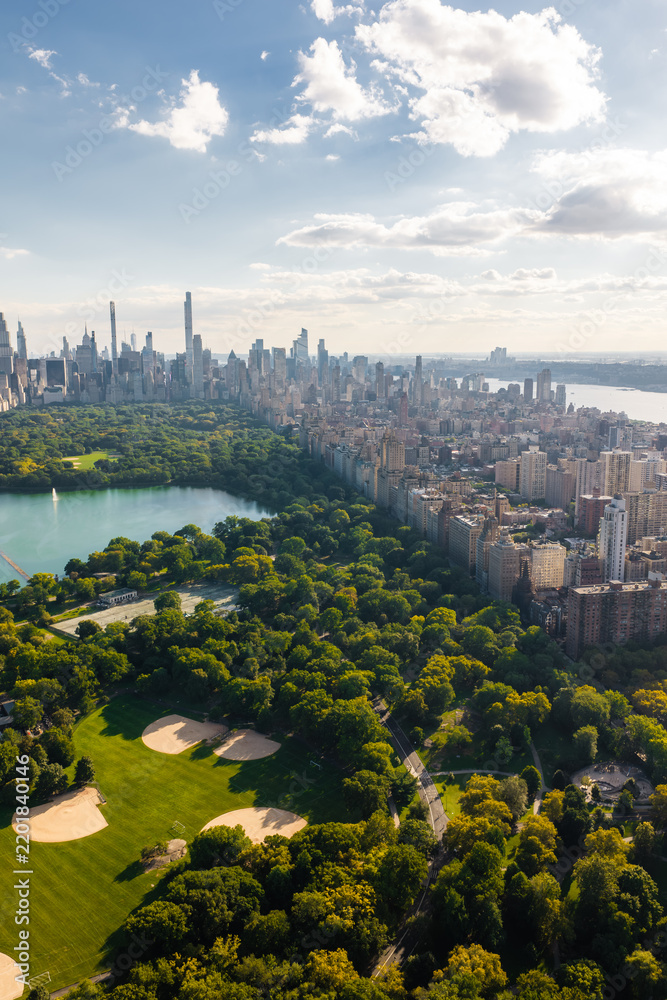 Obraz premium Aerial view shows Central Park featuring baseball fields and the Jacqueline Kennedy Onassis Reservoir beside the Manhattan skyline along the Hudson River in New York.