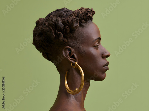 A sculpture of a woman adorned with sizable gold hoop earrings on a green backdrop
