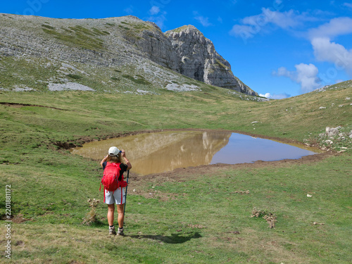 Female hiker taking a picture of Monte Murolungo mountain peak with a small lake reflection in Lazio, Italy
