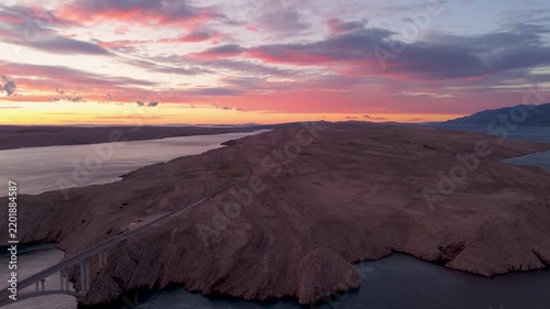 Cinematic aerial drone view of Pag Bridge in Croatia at sunset, featuring the dramatic rocky landscape of Pag Island, Adriatic Sea, rugged coastline, and warm golden evening light