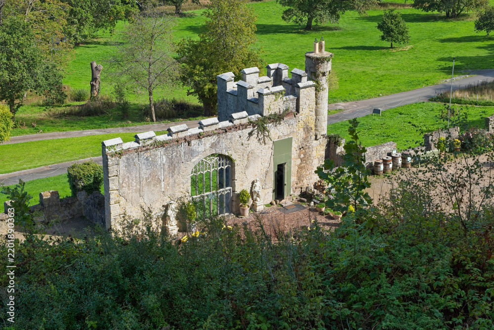 Fototapeta premium A small, weathered stone castle folly featuring a modern window and crenellated tower, nestled within a lush green park landscape - Gwrych Castle, Abergele, Wales, UK