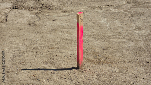 Wooden construction survey stake painted neon pink driven into dry barren dirt ground with hard shadows