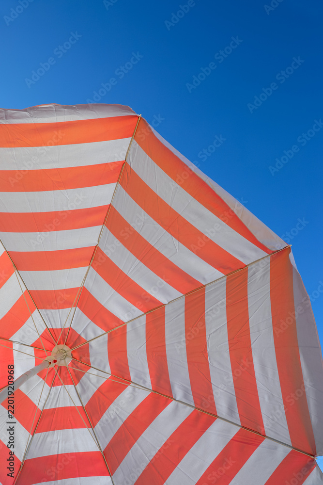 Obraz premium One striped beach umbrella under blue sky, bottom view