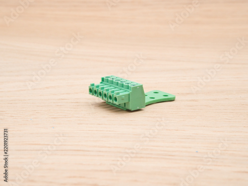Green Electrical Terminal Block on Wood - A close-up view of a green plastic electrical terminal block with multiple screw-down connectors, resting on a light wooden background.