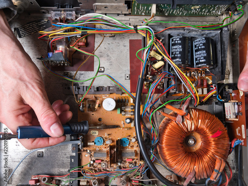 Electronic Device Internal Components - A hand points at the intricate toroidal transformer inside an electronic device, revealing wires, circuits, and capacitors.