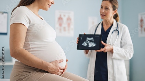 A woman is sitting on an exam table holding her belly while a doctor holds an ultrasound image and talks to her in a medical office during a prenatal visit.