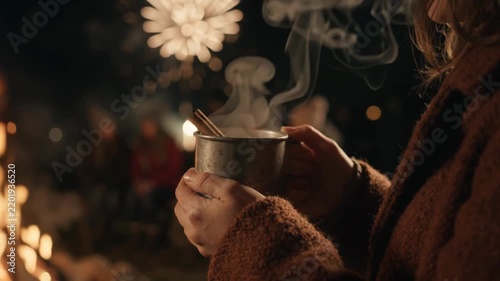 Cozy mulled cider by bonfire light on chilly evening with steaming cup in hands near fire. Cozy atmosphere creates warmth as friends gather around. Concept of Guy Fawkes Night celebration.