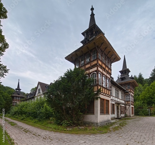 Historic villa complex with ornate timber towers and overgrown courtyard entrance