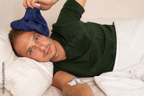 Sick Man with IV Cannula and Cold Compress Resting in Bed