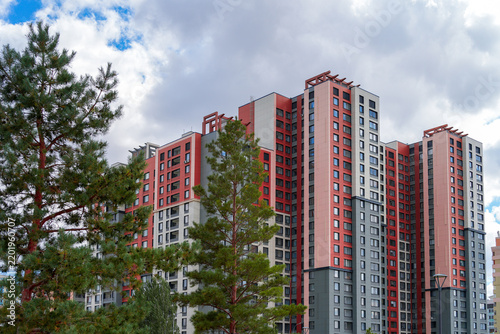 Modern multi-story residential apartment buildings with red and white facade against cloudy sky. Real Photo
