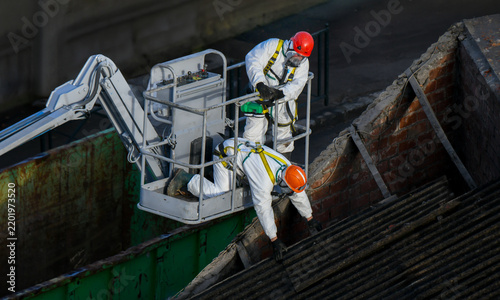 Fotografie Ouvriers en combinaison de protection déposant des plaques de toiture en fibroci