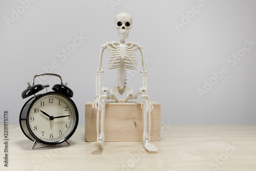Obraz na płótnie Skeleton Figure Waiting Beside Alarm Clock With Copy Space