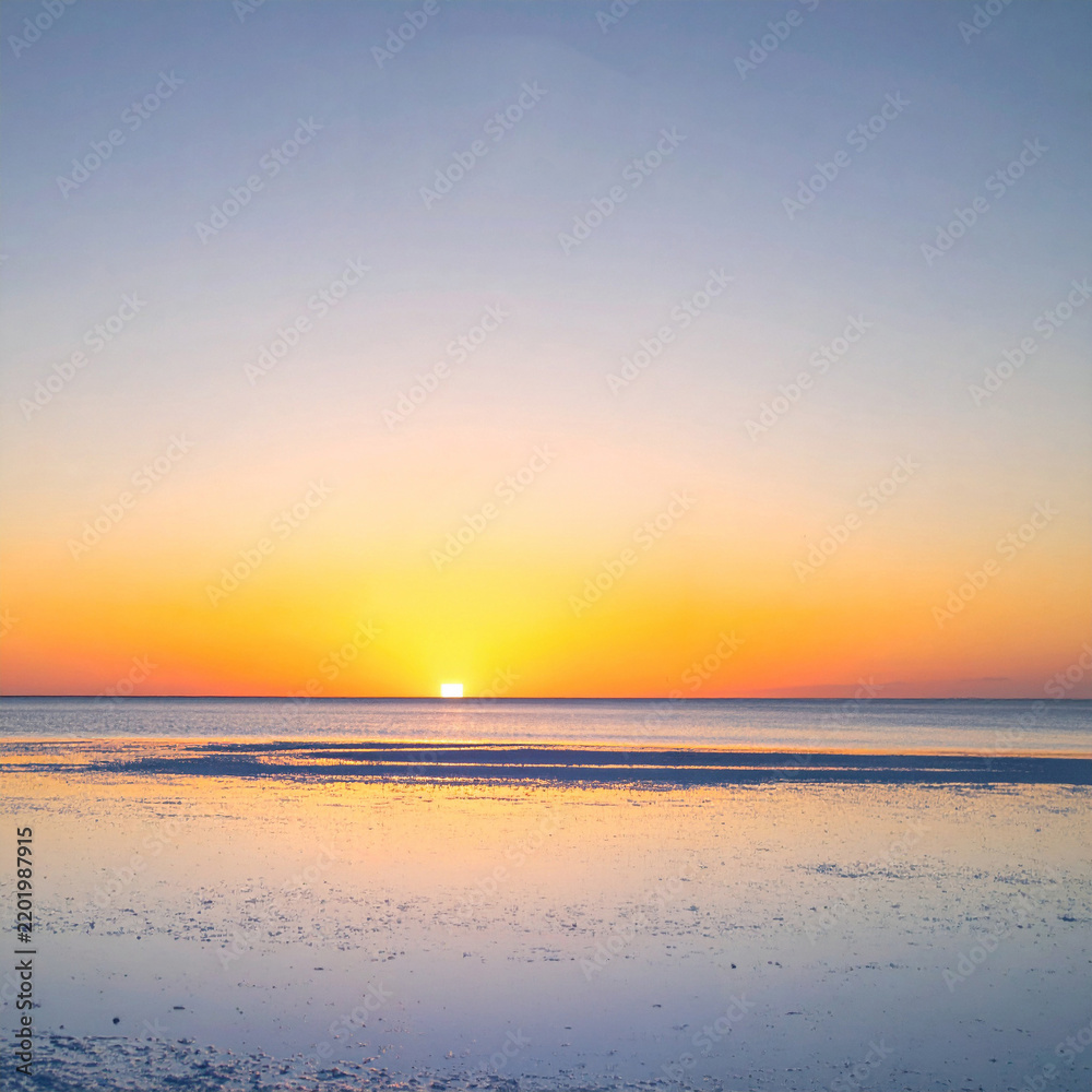 Fototapeta premium A breathtaking sunset over a salt flat, casting golden light on the reflective surface. This peaceful, minimal landscape features no people, evoking serenity and hope for travel and wellness.
