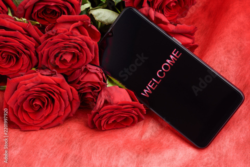 Smartphone with Welcome Text on Screen Lying on Red Roses Bouquet