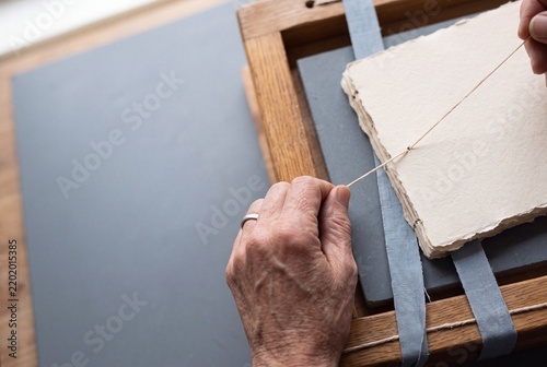 Hands of an artisan bookbinder sewing handmade paper signatures using traditional wooden frame and thread