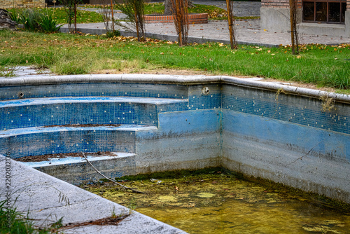 Abandoned pool shows cracked tiles and green algae