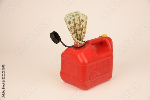 Paper currency in pour spout of gallon gas can on white background, conceptual image depicting the high cost of gasoline.