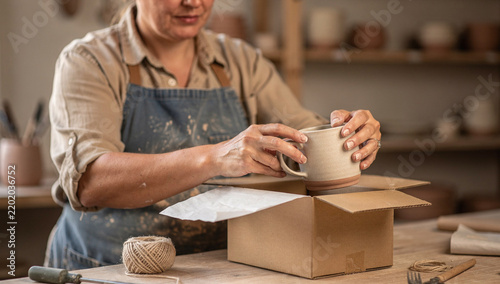Handmade terracotta mug being lowered into kraft shipping box