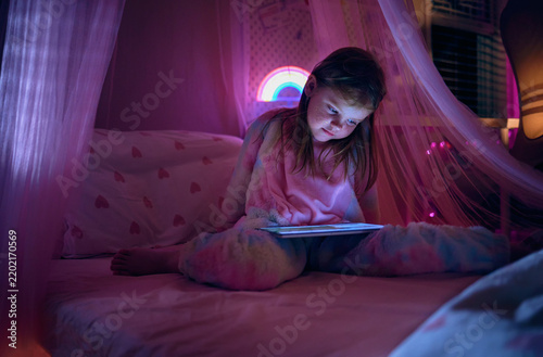 Konstfotografi Young girl using tablet in bed at night illuminated by screen light