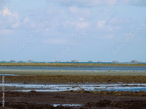 Obraz na płótnie An expanse of rock and mud exposed at low tide, with fishermen's fishing platforms in the background