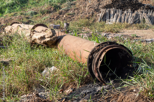 Large rusty industrial steel pipes at an outdoor construction site. Old, rusty steel pipes in an open area near a tree trunk.