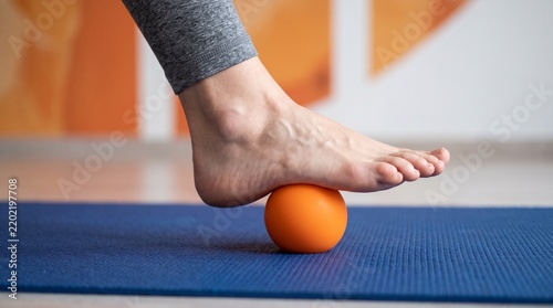 A person's bare foot uses an orange massage ball on a blue yoga mat for self-care and muscle relief plantar fasciitis