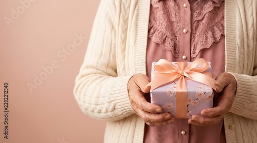 Elderly woman holds beautifully wrapped lavender gift box adorned with delicate cherry blossom print and satin peach ribbon as heartwarming gesture of love.