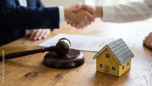 Legal and client shaking hands after closing real estate transaction with wooden gavel and miniature house model on wooden desk