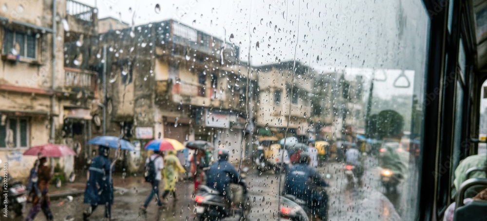 Obraz premium Monsoon city life and everyday urban mobility in India, featuring rainy streets, pedestrians, public transportation, traffic, umbrellas, wet glass, and atmospheric urban surroundings.