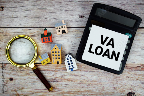 VA Loan text with house model, calculator and magnifying glass on wooden background