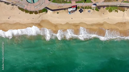 Static top down drone view of turquoise Pacific waves rolling onto a sandy beach beside the coastal promenade of Viña del Mar, Chile.