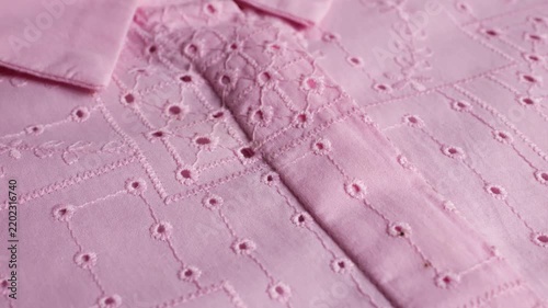 A close-up of a pink cotton women's shirt features delicate eyelet embroidery, batiste material texture, needlework patterns, elegant light color, traditional geometric lace, and sewing art.