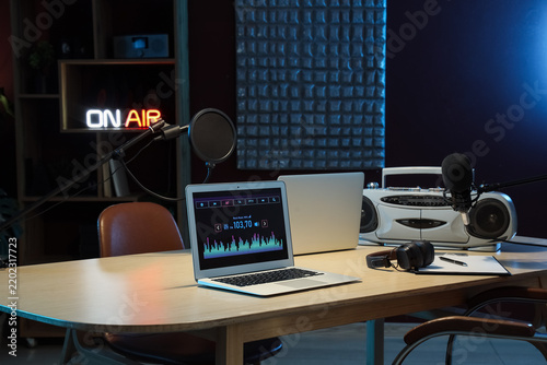Laptops with boombox and headphones on table in dark radio studio