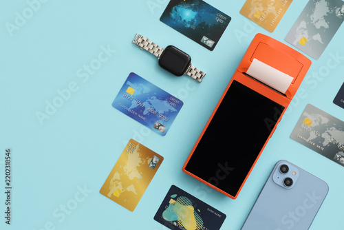 Payment terminal with credit cards, smartwatch and mobile phone on blue backg...