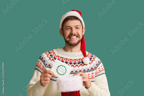 Happy young man in Santa hat with Christmas greeting card and sock on green b...