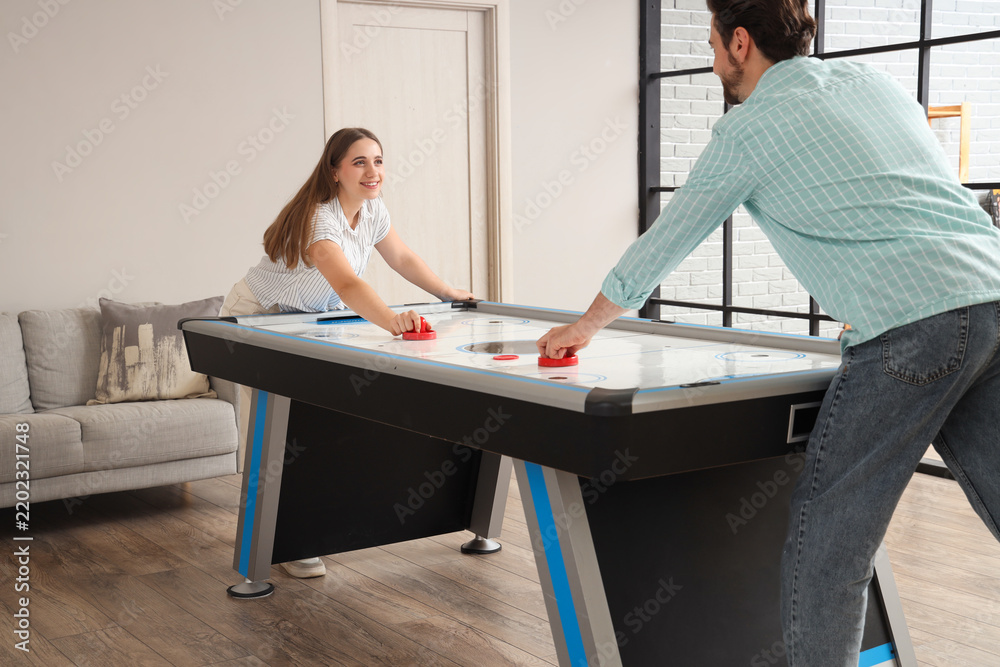 Obraz premium Young woman with her husband playing air hockey at home