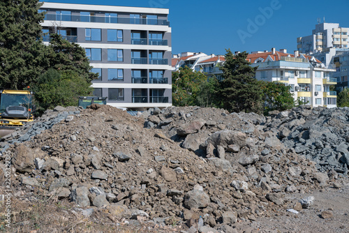 Konstfotografi Mounds of excavated earth, grey crushed rock, and demolition rubble dominate an active development lot in front of modern and older residential apartment buildings