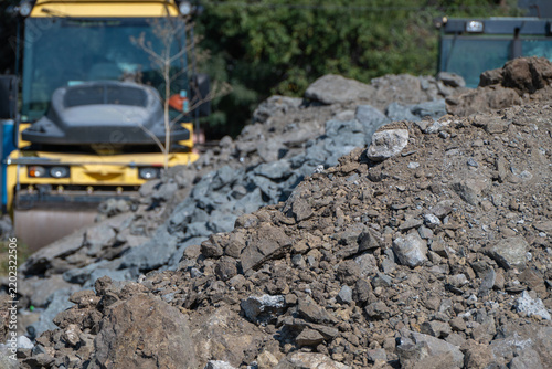 Konstfotografi Mounds of coarse excavated dirt and crushed rock dominate the foreground with a yellow road roller compactor operating at a construction site in the background