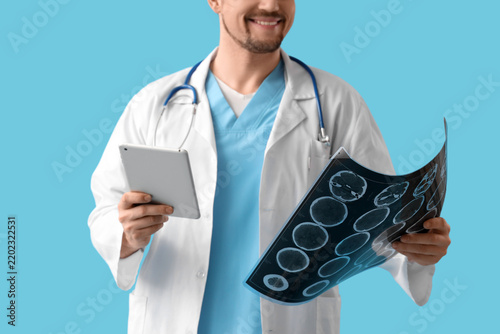 Male doctor with MRI scan and tablet computer on blue background, closeup