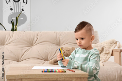 Little boy drawing with felt-tip pens on table at home