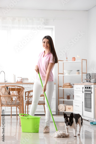 Young woman with her French bulldog mopping floor in kitchen