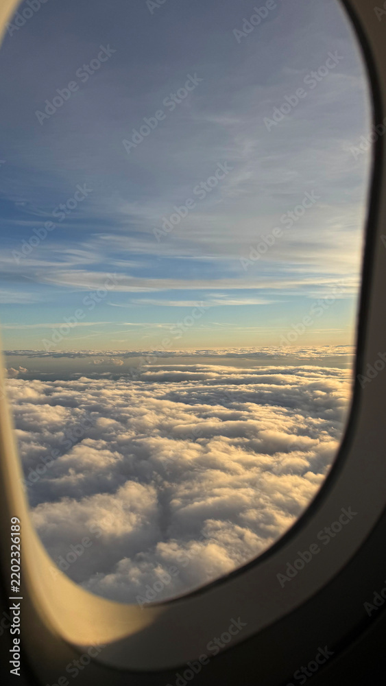 Obraz premium Beautiful scenic view of fluffy white clouds and blue sky at sunset through an airplane window frame during a commercial flight, travel wanderlust and dream destination concept