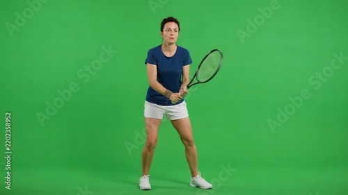 Young male tennis player standing alert with racket against a bright green studio background, ready for a forehand stroke