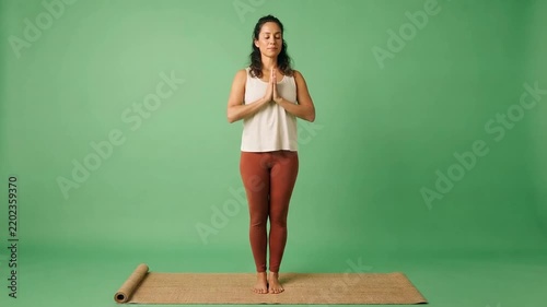 Young woman practicing yoga meditation in prayer pose on a rolled mat against a green studio background