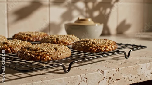 Golden sesame coated vegan cookies cool across a raised black wire rack on a pale stone counter, framed by warm shadows, a ceramic bowl, toasted seed texture, and quiet artisanal kitchen atmosphere