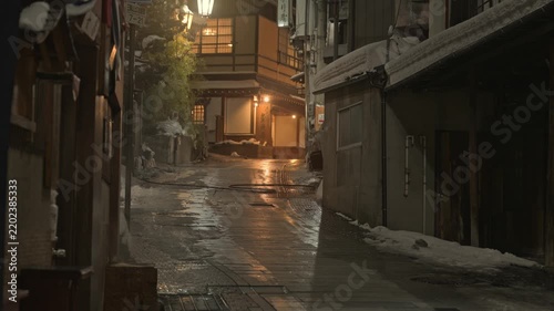 提灯の温かい明かりが灯る雪の温泉街の夜の石畳スローモーション