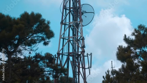 A large telecommunications and broadcasting lattice tower with multiple antennas that sits on the mountain peak in the center against the background of a blue cloudy sky
