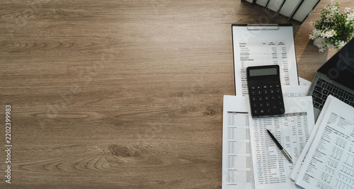 Fotografie Accounting workspace with calculator, financial reports and laptop on wooden desk with wide copy space, showing accounting analysis, bookkeeping and business finance planning