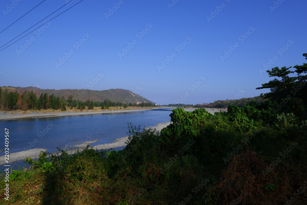Obraz premium Natural Mountain View with Rocky Riverbank and Forested Hills