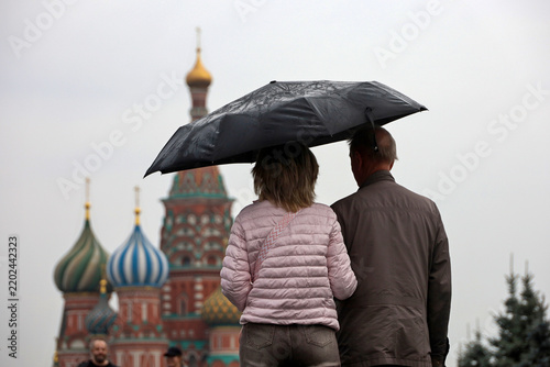 Autumn rain in Moscow. Couple with one umbrella walking on the Red Square on background of St. Basil's Cathedral